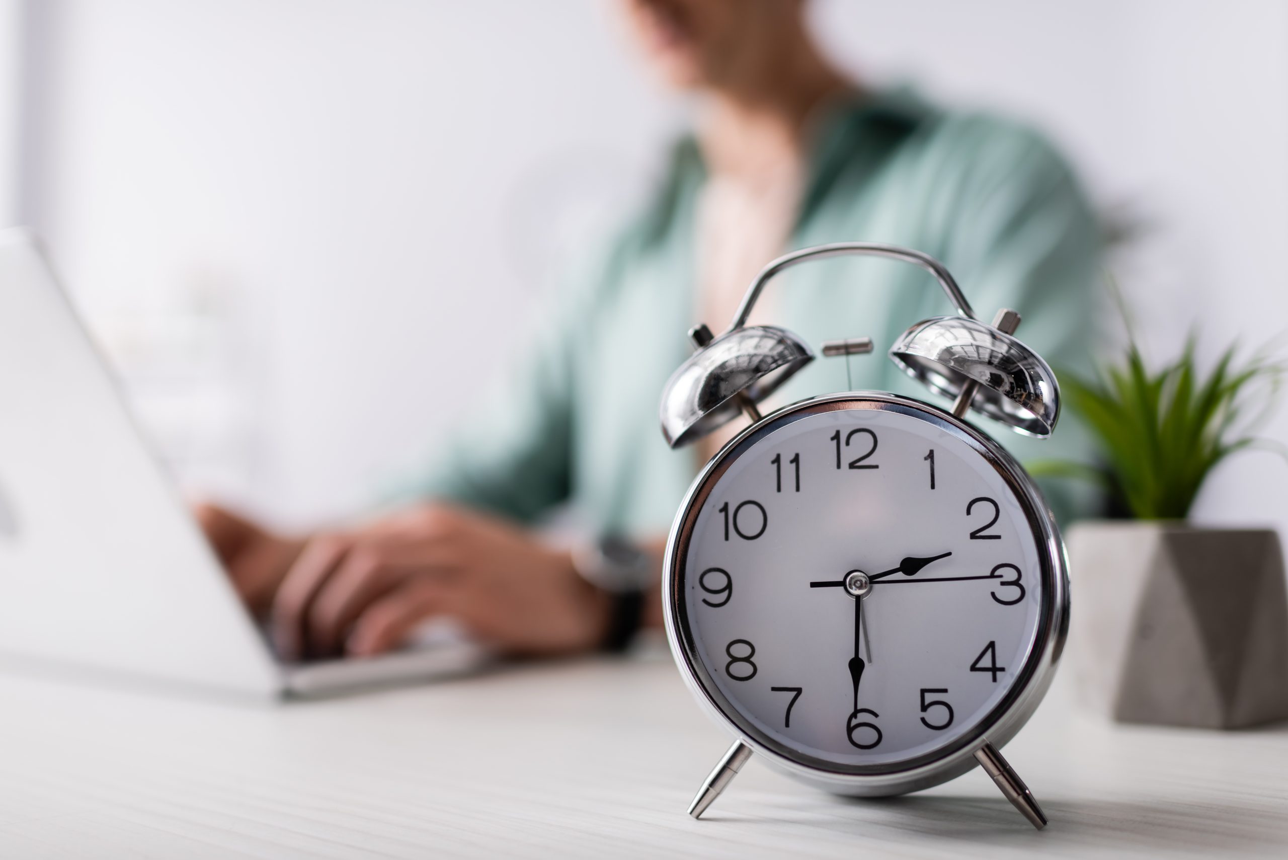 Selective focus of alarm clock on table near man using laptop at